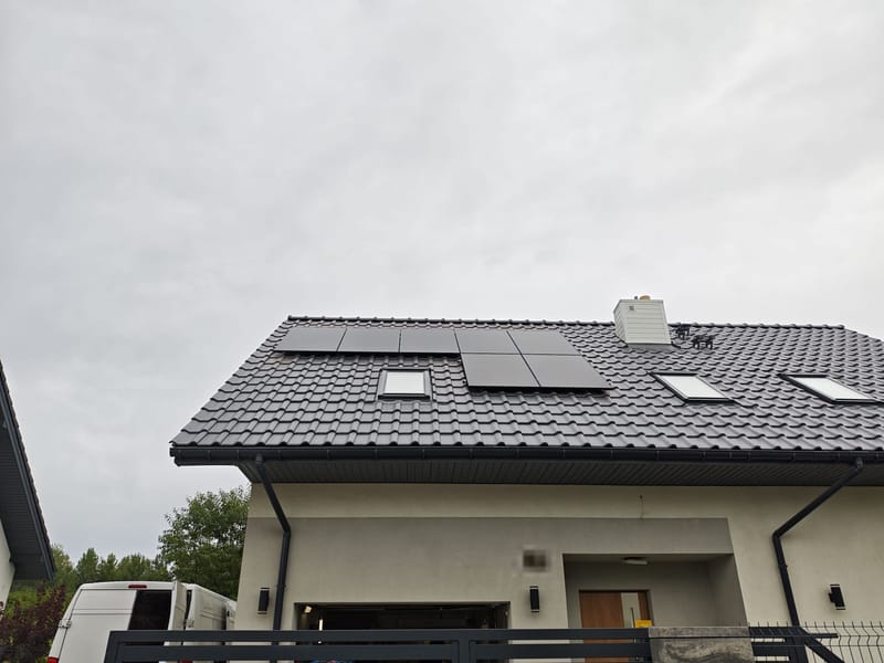 Panele fotowoltaiczne rozmieszczone między oknami dachowymi — widok od frontu domu